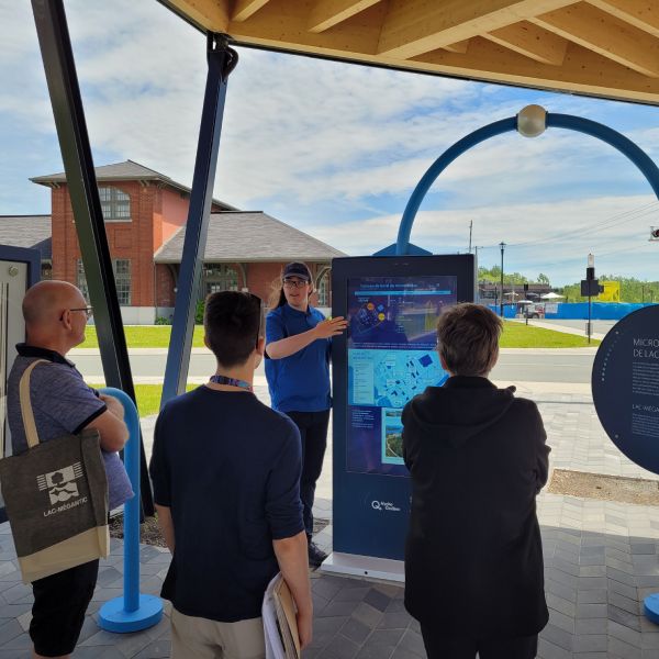 A tour guide presents the interactive terminal under the multipurpose solar-powered covered structure.
